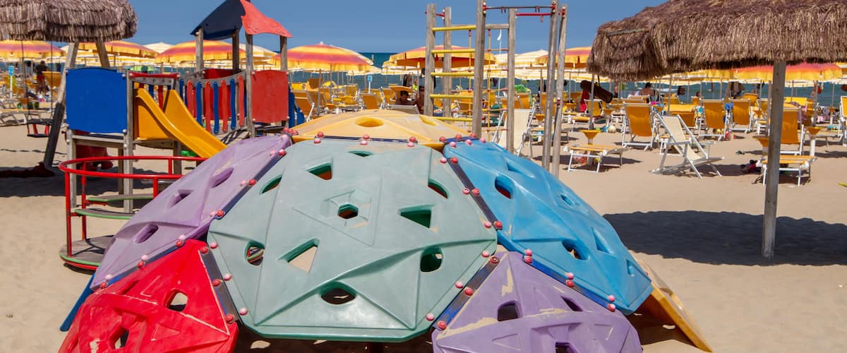 A beach play area with colorful climbing structures and thatched umbrellas.