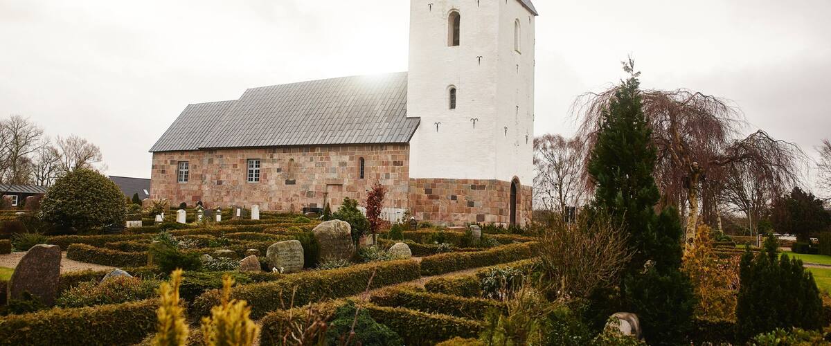 A church with a tall tower and a cemetery in front.