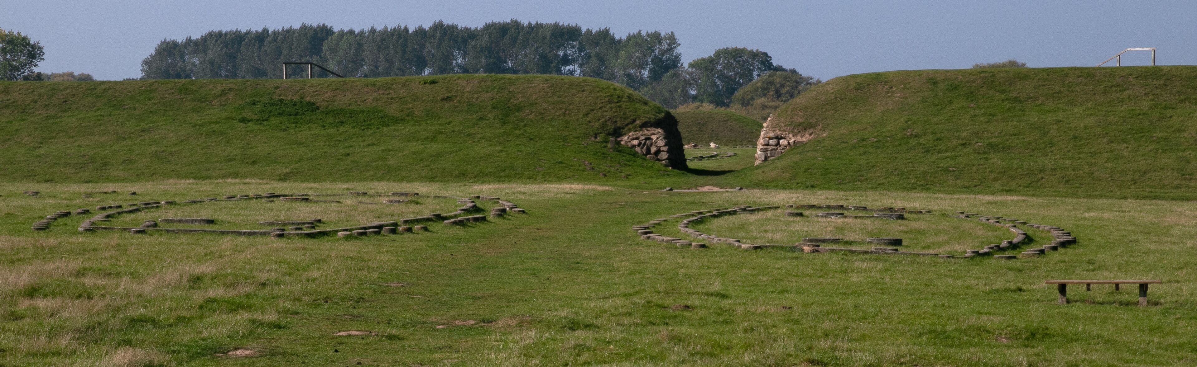 A grassy field with ancient stone structures and a wooden bench.