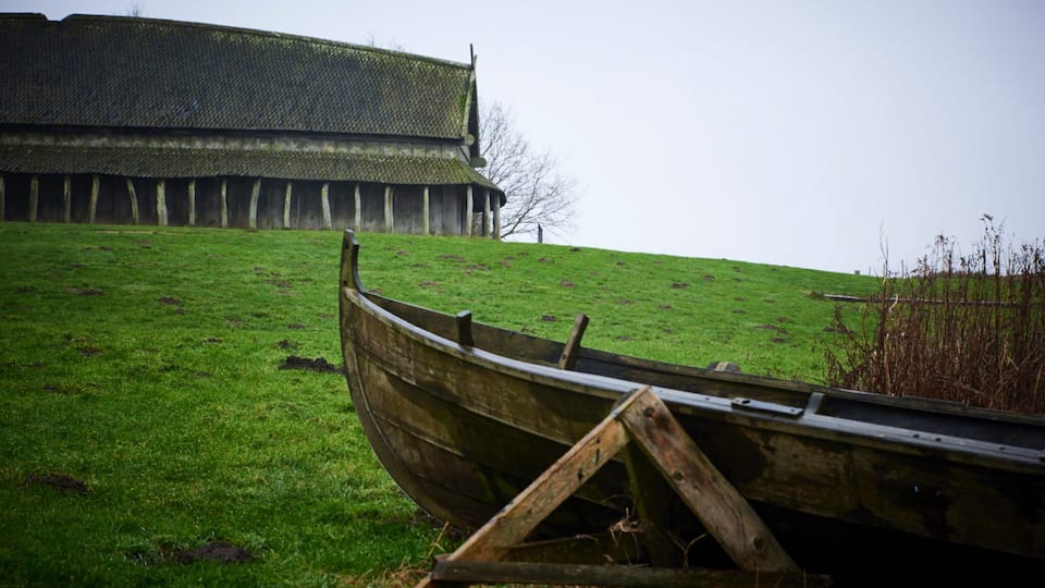 A wooden boat on a grassy hill with a large building in the background.