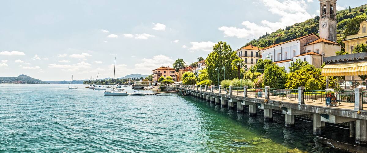 A waterfront town with a prominent church tower, a pier, and boats docked along the calm water.