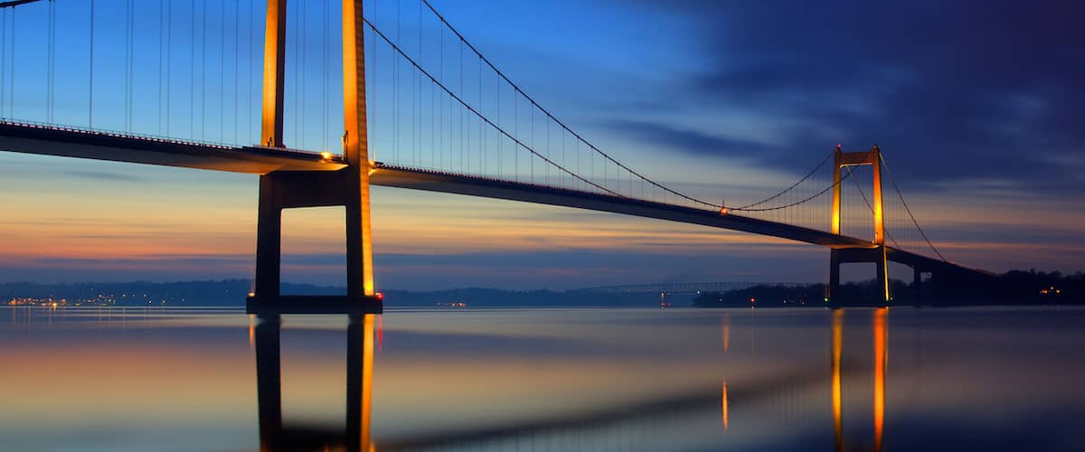 A suspension bridge at dusk with its reflection on calm water.