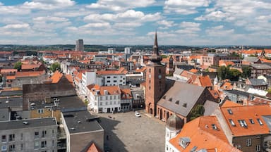 Paisagem urbana com telhados de telha vermelha, uma torre de igreja imponente e um céu azul claro.
