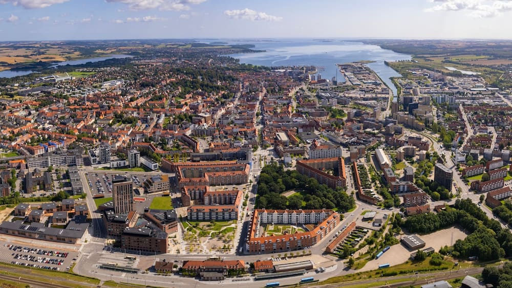 Oversigtsbillede af en by med en flod, grønne områder og en blanding af boliger og erhvervsbygninger.