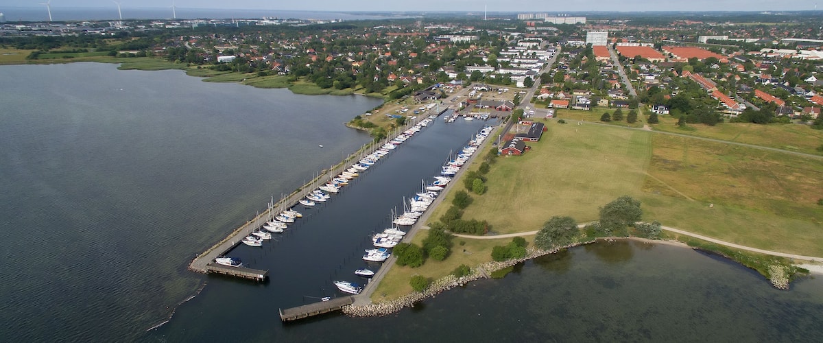 An aerial view of a marina with boats docked, a pier, and a town in the background.