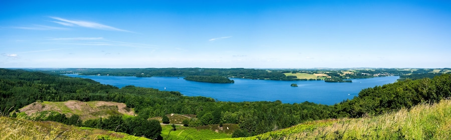 Un lago circondato da colline boscose e un cielo azzurro limpido.