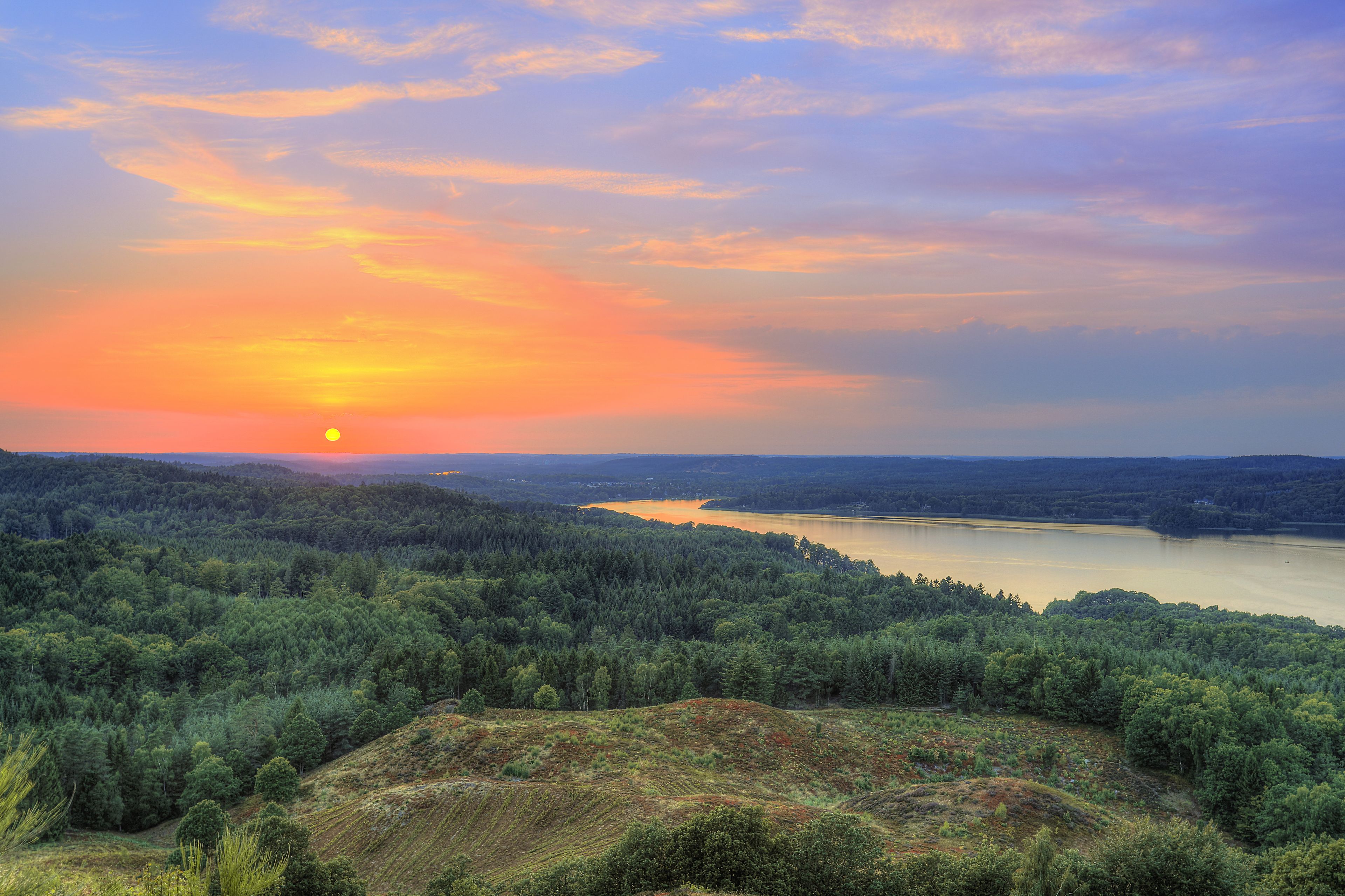 A sunset over a forested landscape with a lake.