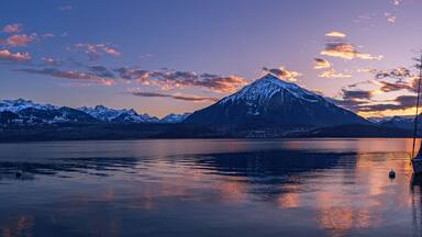 Una montaña al atardecer con un velero en un lago tranquilo.