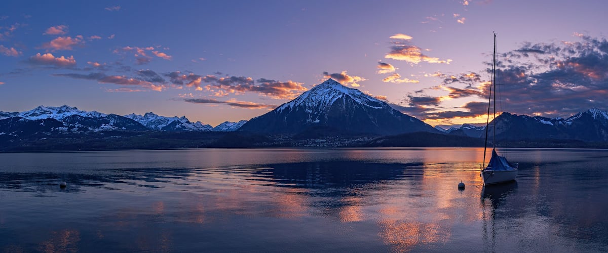 A mountain at sunset with a sailboat on a calm lake.