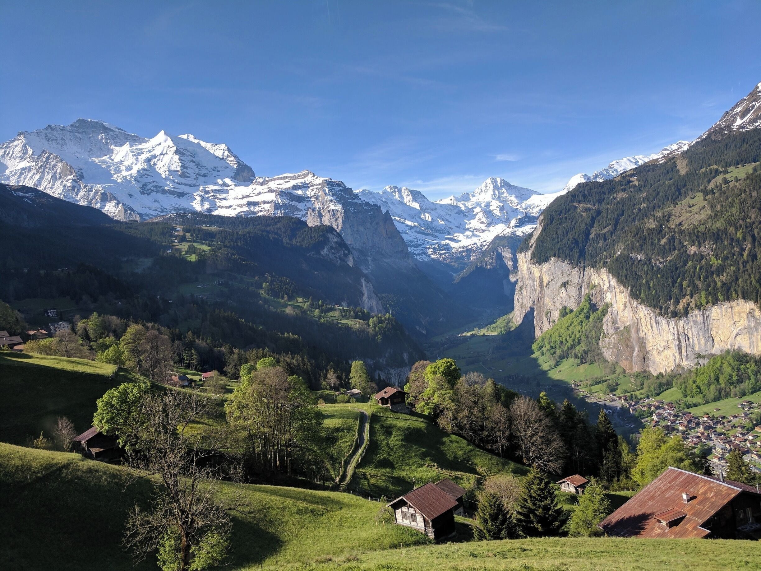 A valley with snow-capped mountains, green fields, and traditional houses.
