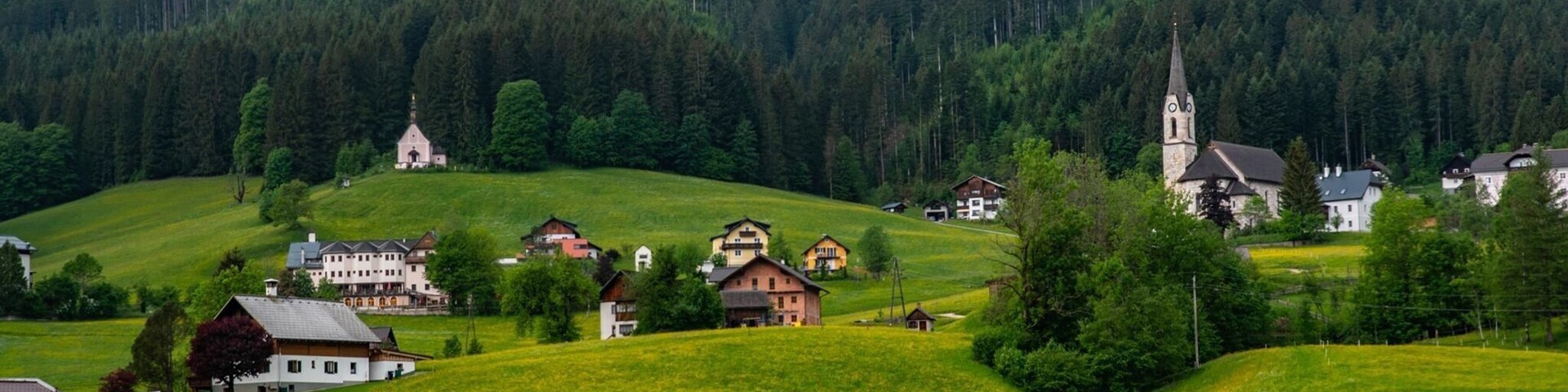 Un pueblo con casas en una ladera, una iglesia y una montaña boscosa.