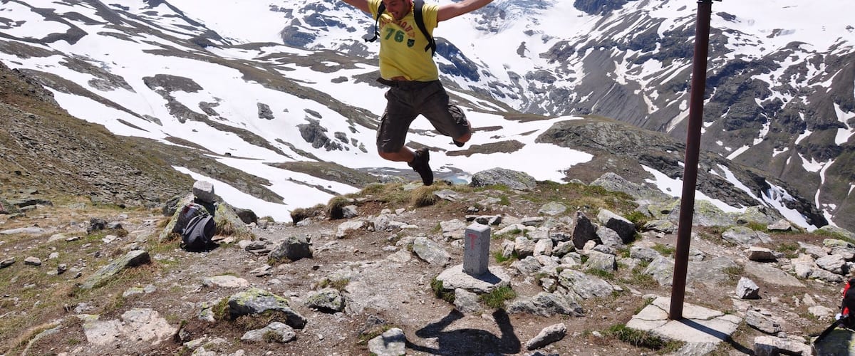 A person jumping in a mountainous area with snow-covered peaks in the background.