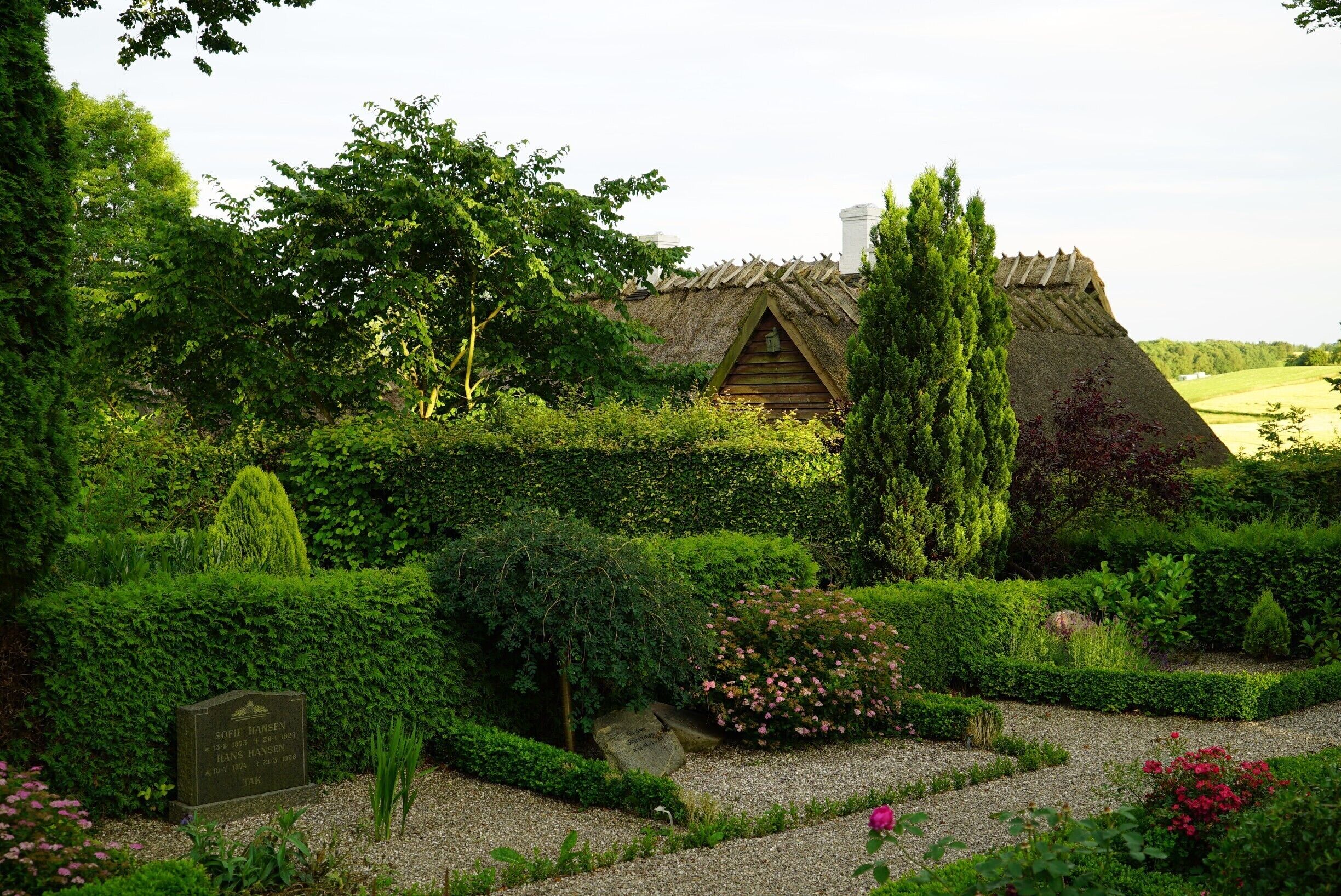 A thatched-roof house surrounded by lush greenery and a well-maintained garden.