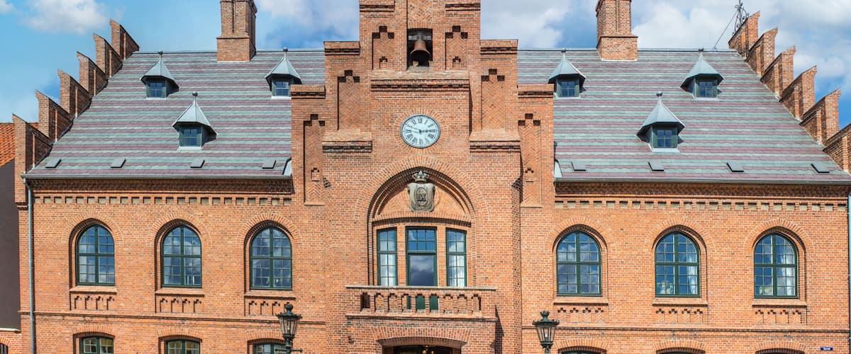 A historic brick building with a clock tower, arched windows, and a flag.