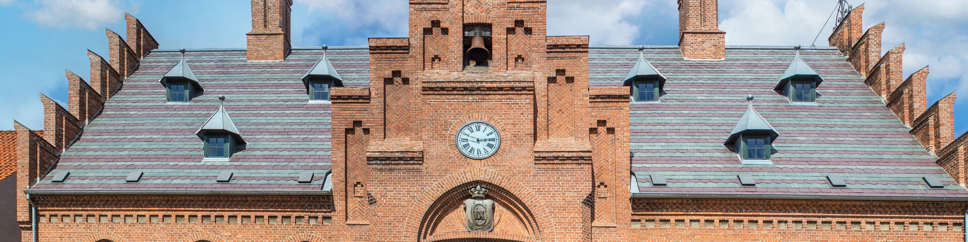 A historic brick building with a clock tower, arched windows, and a flag.