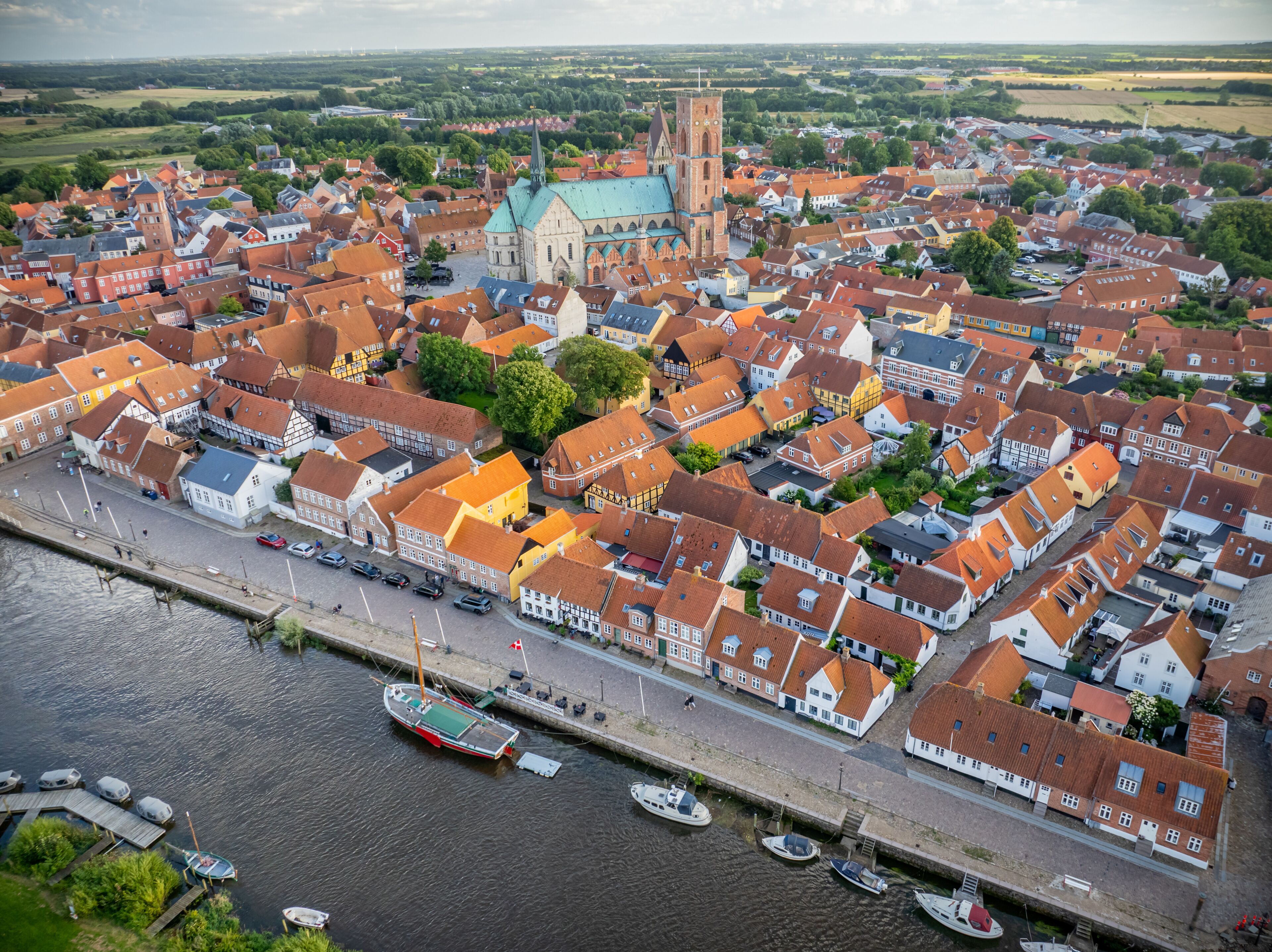 Aerial view of historic town Ribe with majestic Ribe cathedral, red-roofed buildings and boats docked along the riverside, set against lush, green landscape, south-west Jutland, Denmark.
