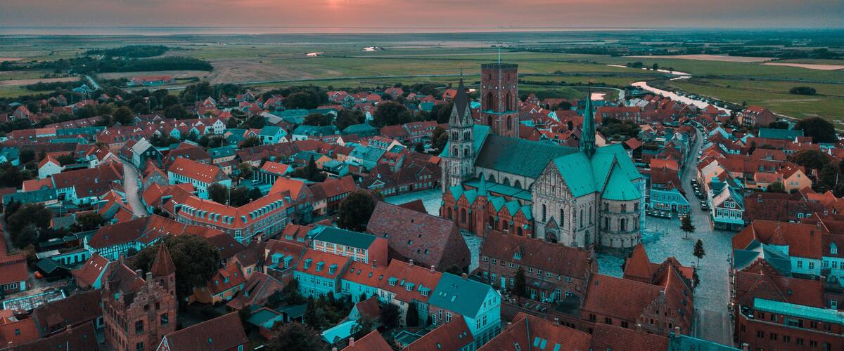 A town with historic buildings, a prominent church, and a sunset over the horizon.