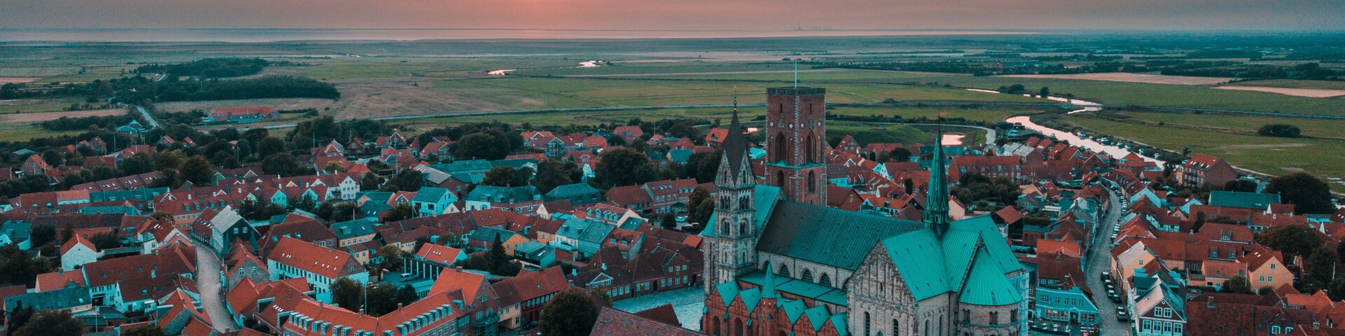 A town with historic buildings, a prominent church, and a sunset over the horizon.