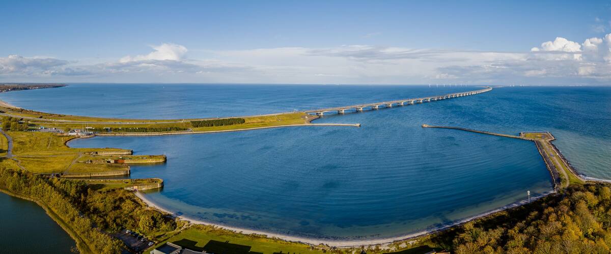 Panoramic view from the coast of Denmark with the Storebælt Bridge spanning across the horizon, connecting the two coasts and lighthouse Knudshoved on the coastline.