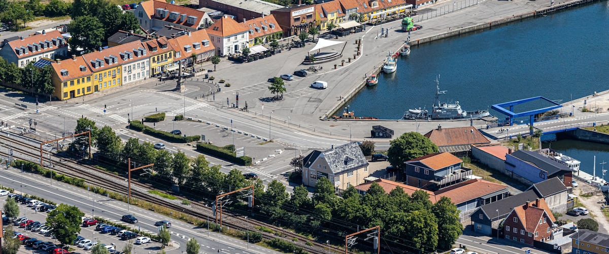 Vista aérea de un pueblo costero con un puerto deportivo, edificios coloridos y una línea de tren.