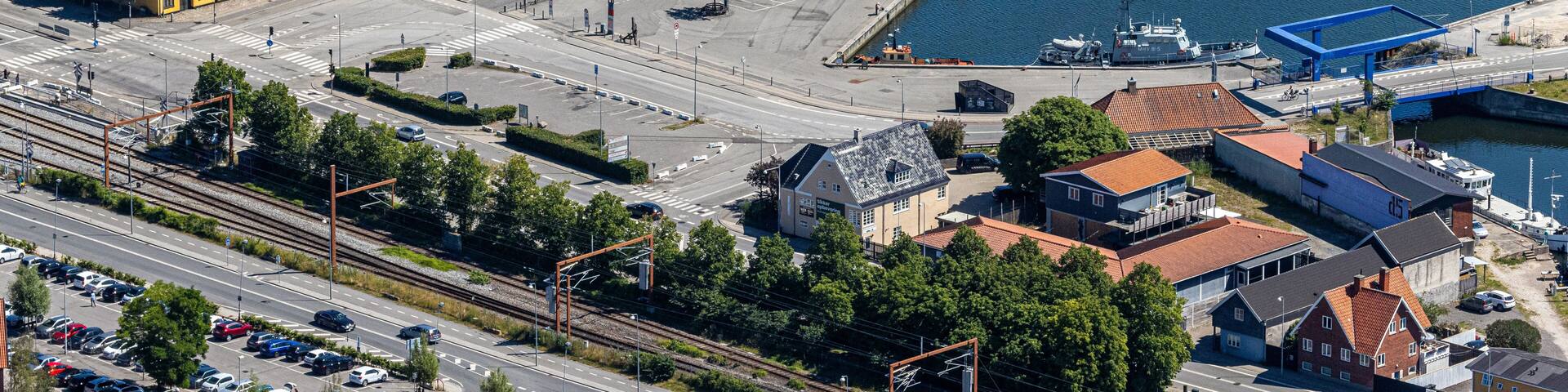 An aerial view of a coastal town with a marina, colorful buildings, and a railway line.