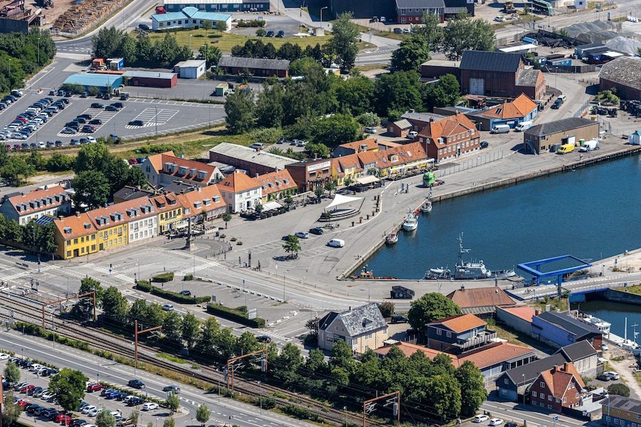 An aerial view of a coastal town with a marina, colorful buildings, and a railway line.