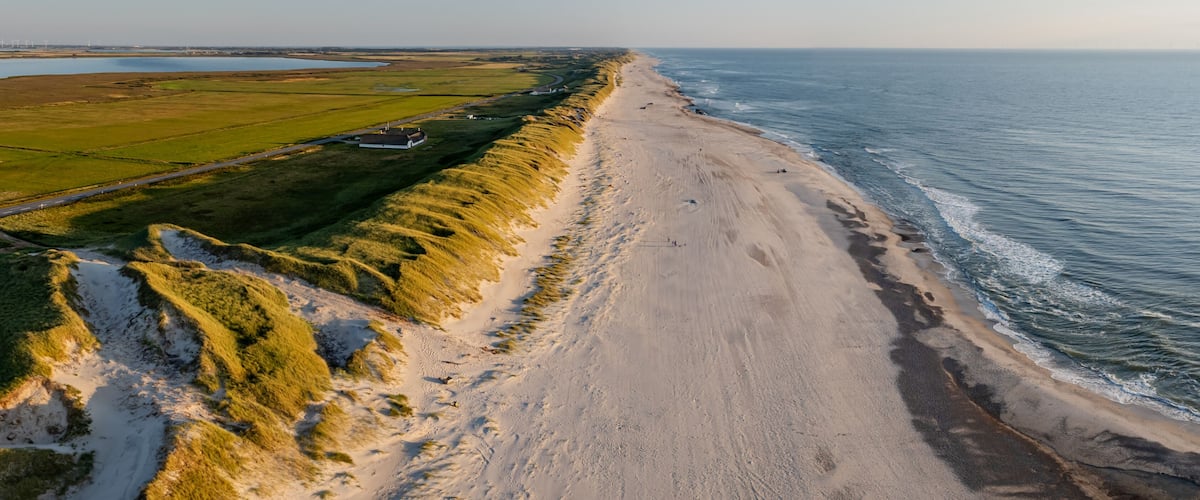 A coastal landscape with a sandy beach, grassy dunes, and a body of water.