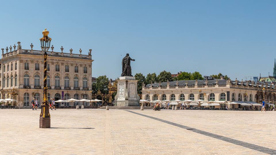A large open square with ornate buildings, a statue, and outdoor cafes.
