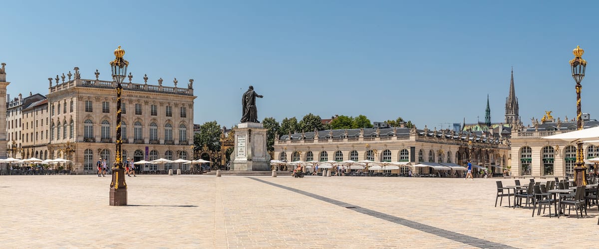 A large open square with ornate buildings, a statue, and outdoor cafes.