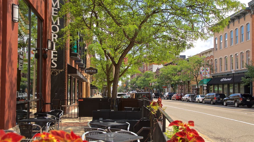 A street with outdoor seating, brick buildings, and cars parked along the road.