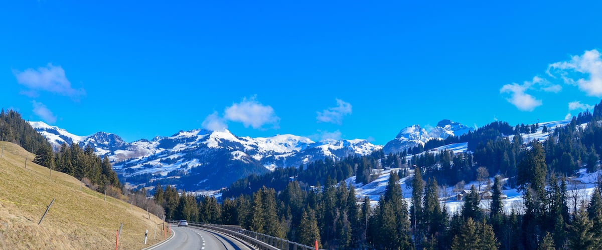 A winding mountain road with snow-capped peaks in the background.
