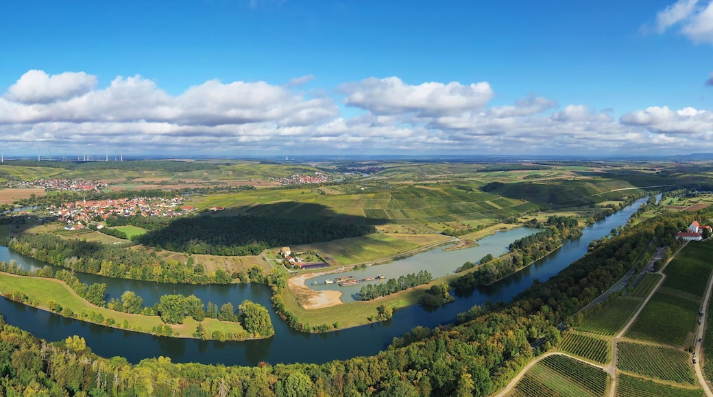 En flod slingrar sig genom en dal med en stad, åkrar och vindkraftverk i fjärran.