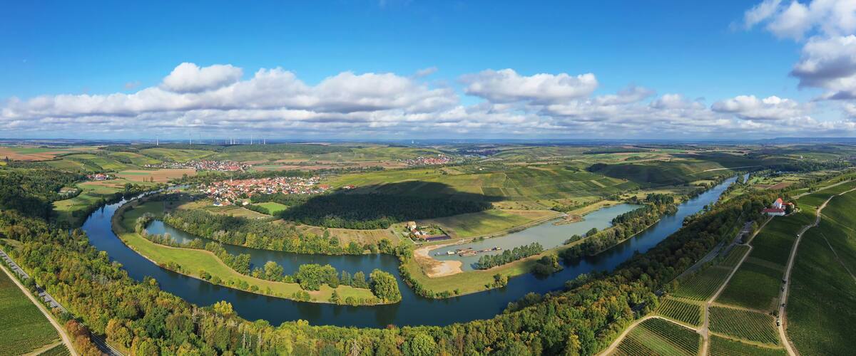 A river winding through a valley with a town, fields, and wind turbines in the distance.