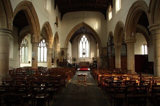 A church interior with arched ceilings, wooden pews, and a central aisle leading to a pulpit.