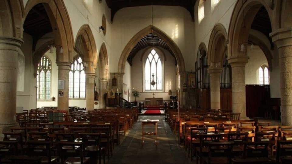 A church interior with arched ceilings, wooden pews, and a central aisle leading to a pulpit.