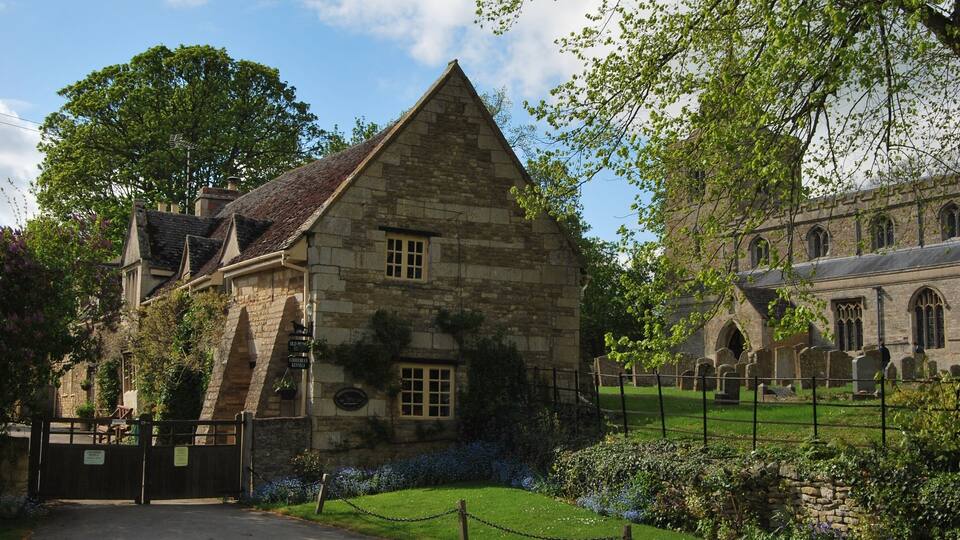 A stone building with a triangular roof, surrounded by a cemetery and a chain-link fence.