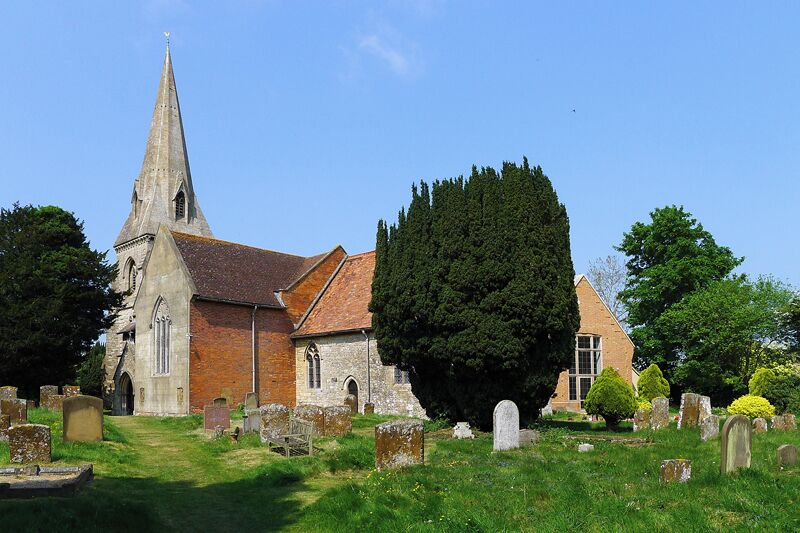 A church with a tall steeple, surrounded by a cemetery with headstones and a large tree.