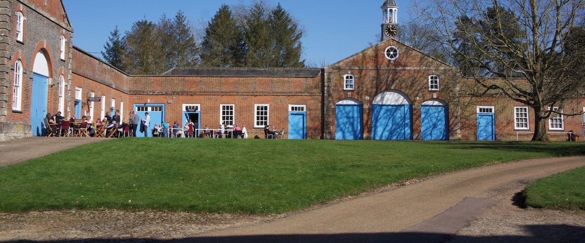 A historic building with a clock tower, a large open courtyard, and a dirt path leading to the entrance.
