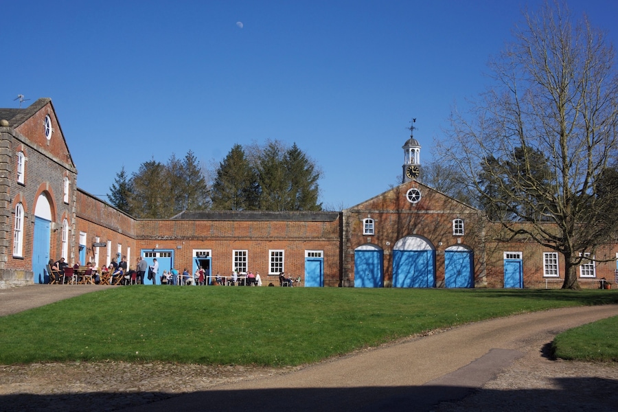 A historic building with a clock tower, a large open courtyard, and a dirt path leading to the entrance.