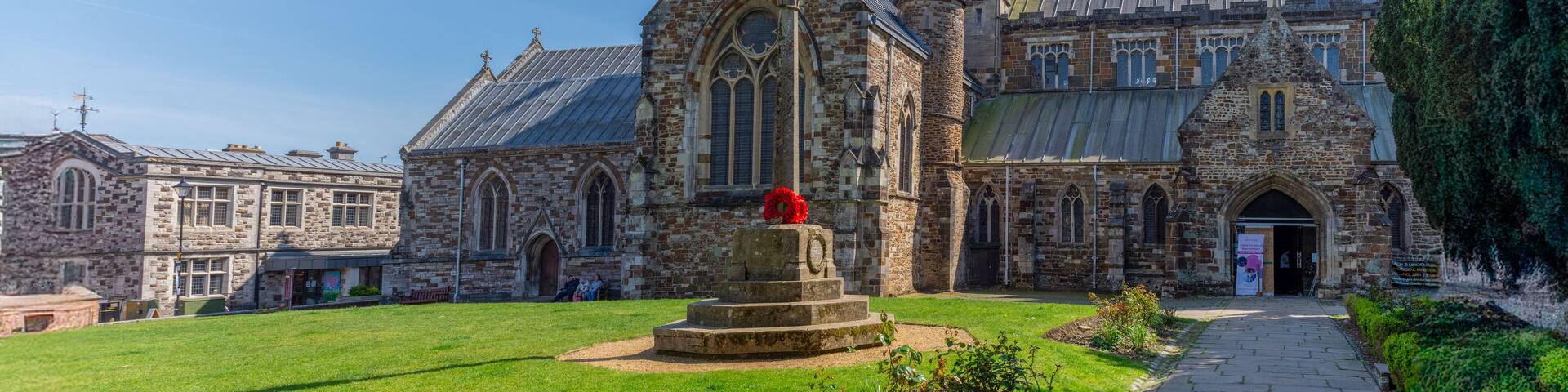 A historic stone church with a prominent tower and a memorial with a red poppy.