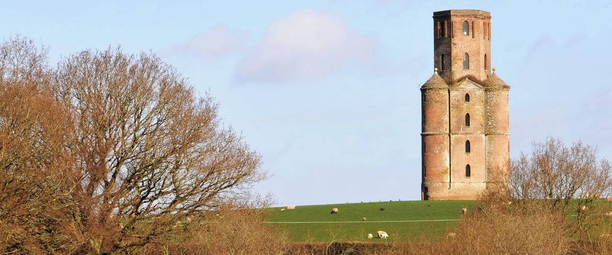 A tower on a hill with sheep grazing below.