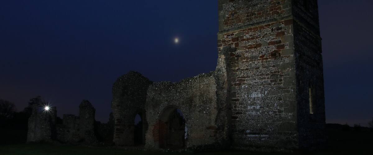 Une structure en pierre d’époque, illuminée par la lumière du crépuscule, avec une lune visible dans le ciel.