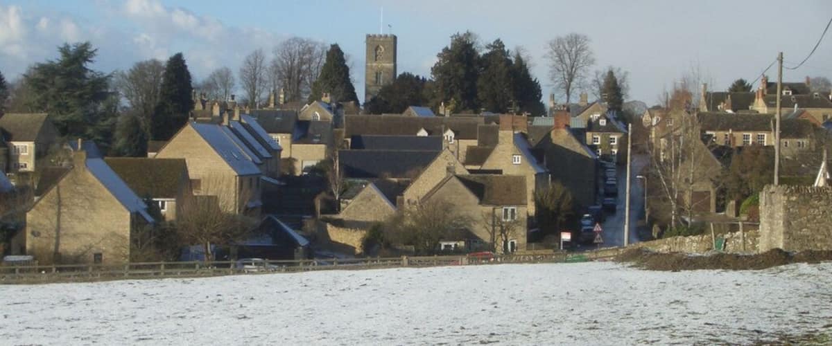 A snow-covered landscape with traditional stone houses and a prominent tower in the background.