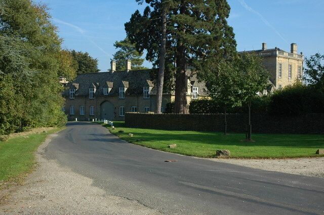 A rural road leading to a large, historic building surrounded by trees and grass.