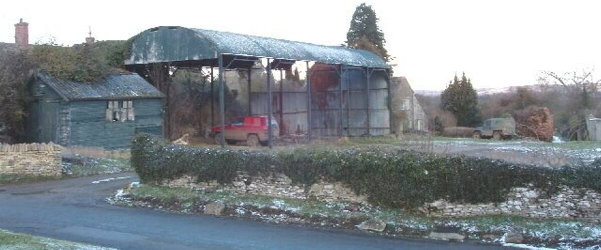 A rural landscape with a metal shed, a red car, and a river.