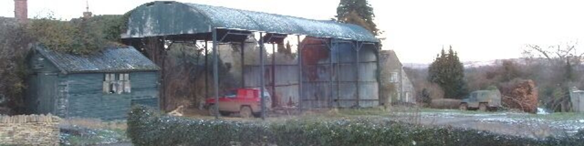 A rural landscape with a metal shed, a red car, and a river.