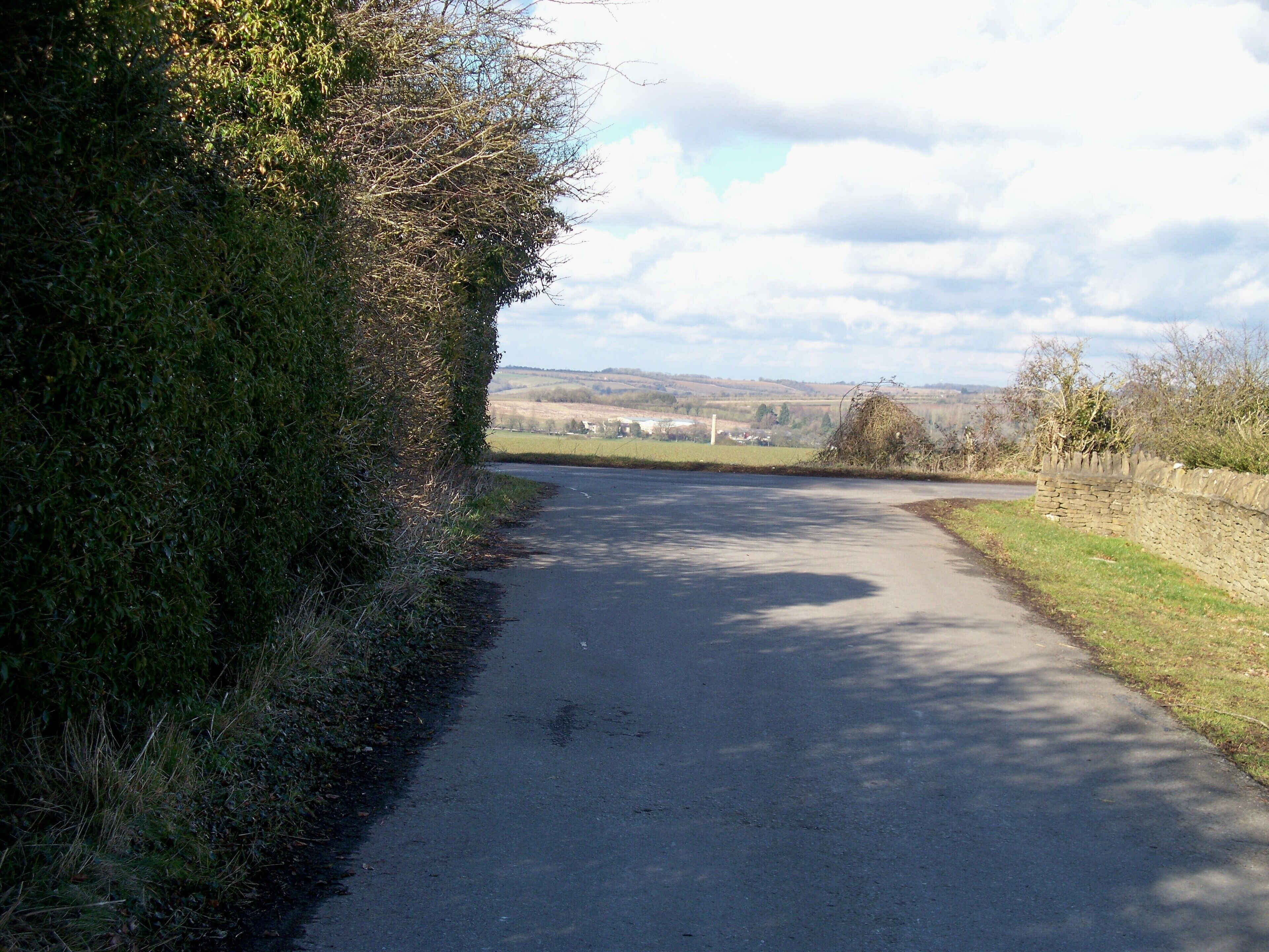 End of the drive. The driveway to Sarsgrove Farm ends where it meets the minor road. The chimney of Bliss Mill can be seen in the distance.