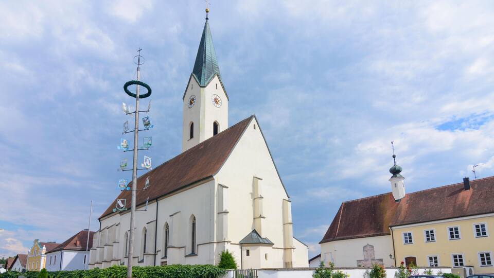 A church with a tall steeple and a clock tower, surrounded by residential buildings and a clear sky.