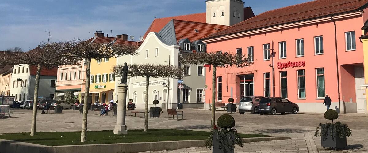 A town square with a prominent church tower, colorful buildings, and a clear blue sky.