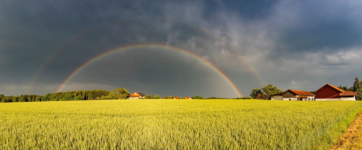 A field with a rainbow, a farmhouse, and a barn.